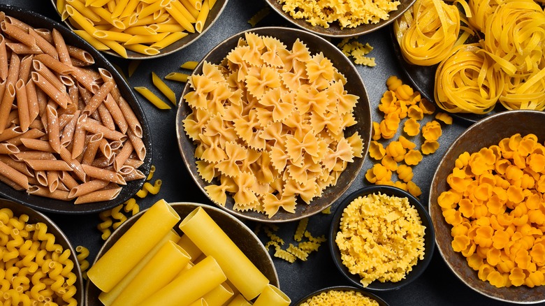 A black table with bowls of various types of pasta.