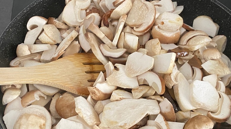 Cooking mushrooms sliced mushrooms with a wooden spoon in a frying pan.