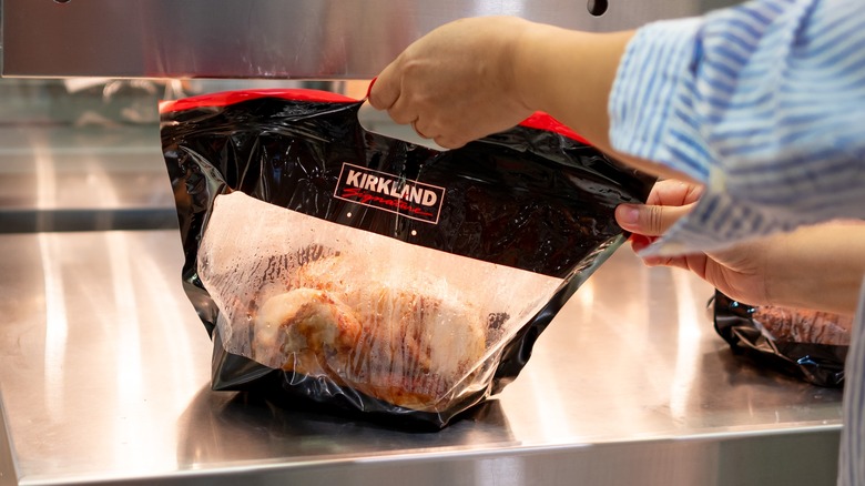 A shopper's hand getting freshly roasted Kirkland Signature Rotisserie Chicken at Costco