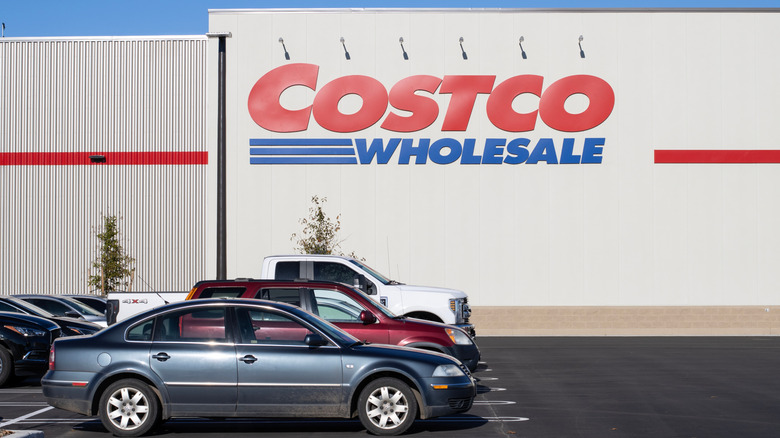A Costco Wholesale store in bright daylight, with emphasis on several cars parked in front of it on the left side of frame