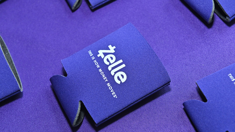 A Zelle branded swag beverage koozie on a purple surface.