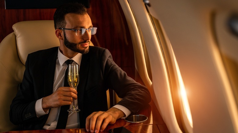 An upper-class man in a suit and tie holding a glass of champagne on a private jet.