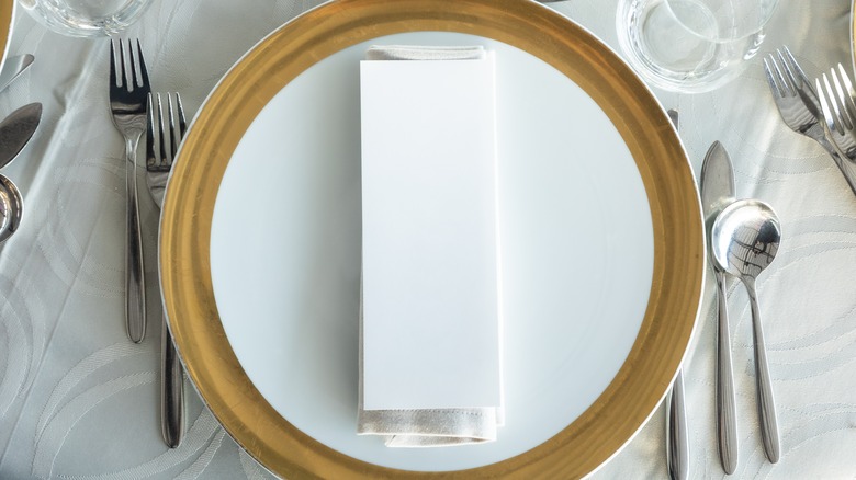 gold-trimmed charger plate under folded napkin surrounded by cutlery