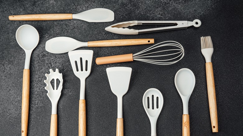 Kitchen spoons, tong, spatulas and other utensils viewed from above on a black counter