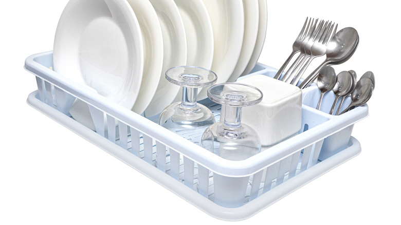 A plastic dish rack holding several plates, two wine glasses, a square dish, and multiple forks and spoons
