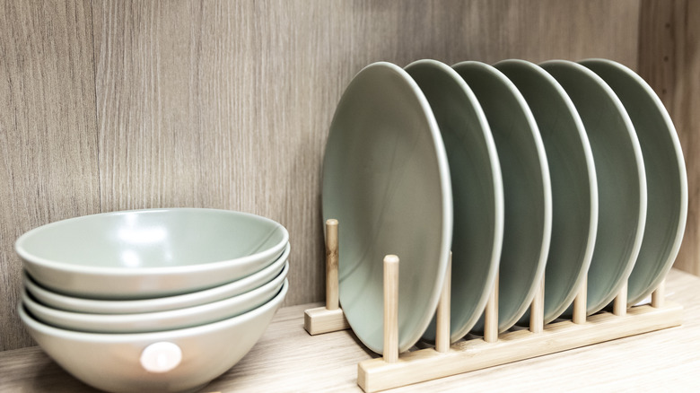 stack of bowls next to several plates upright in a rack, all stored in open cabinet