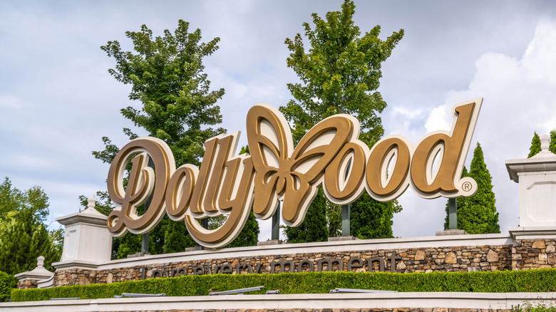 A gold sign that says "Dollywood" where the "W" is a butterfly with trees in the background.