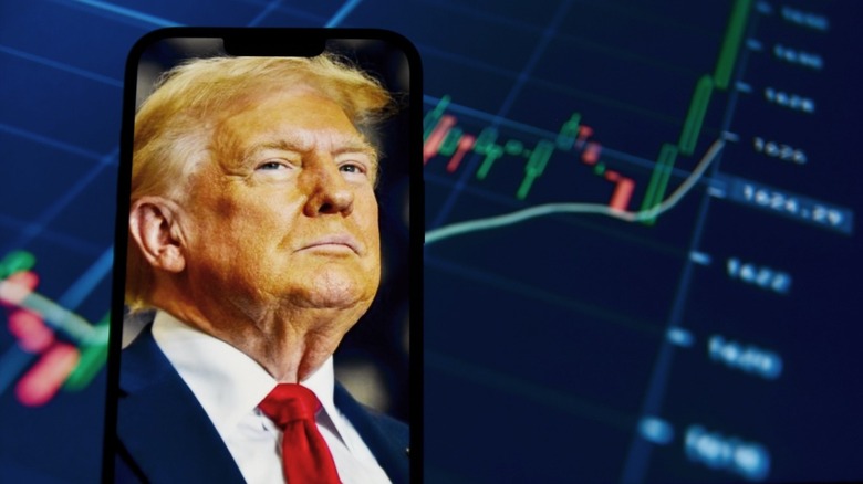 Trump's face on a smartphon held in front of a stock market fluctuation chart.
