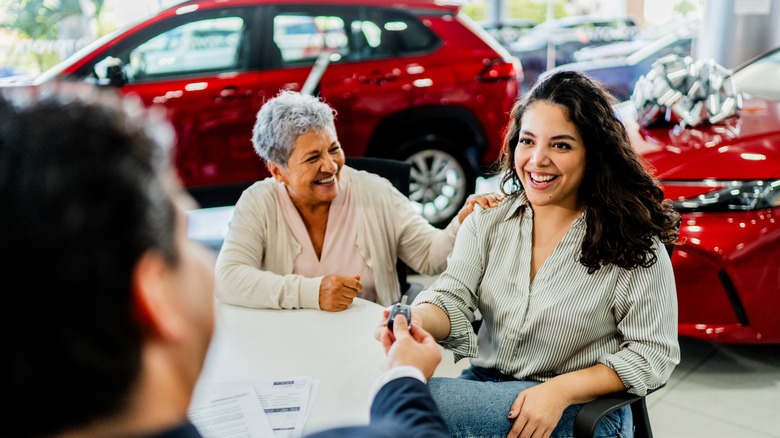 Woman getting keys from salesperson at car dealership.