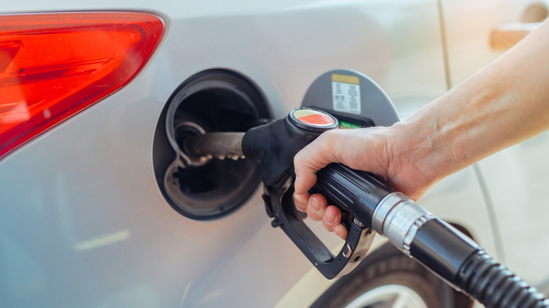 A person refueling a car at a gas station fuel pump.