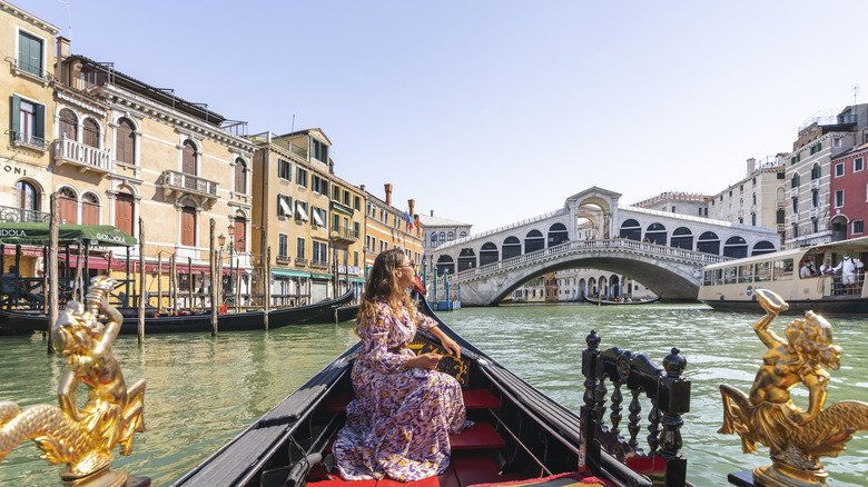 A Millennial woman sightseeing from a gondola on a Venetian canal.