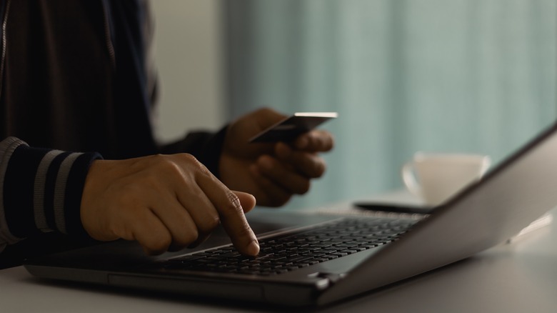Customer is hand paying for service subscription with credit card on laptop at home office