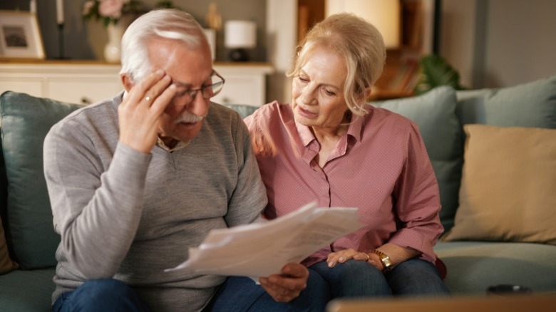 Two senior citizens looking over financial documents in their living room and looking stressed out.