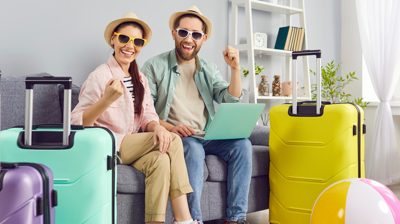 Two delighted travelers with bags packed giving a triumphant fist in the air