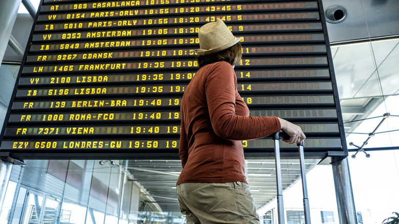 A person in the airport in front of the flight information display.
