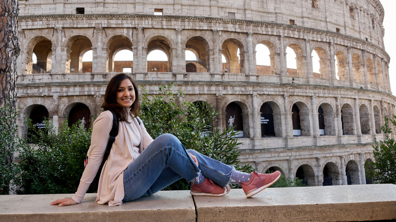 Young woman enjoying her trip to Rome, sitting and smiling near the colosseum