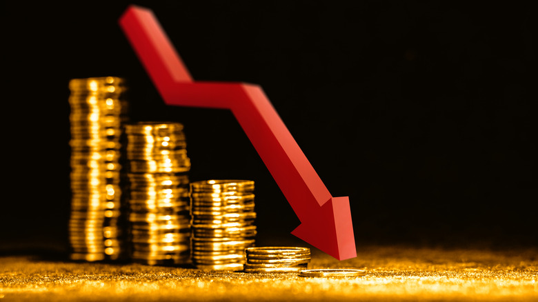 Gold coins isolated on a black background with a red arrow pointing downward