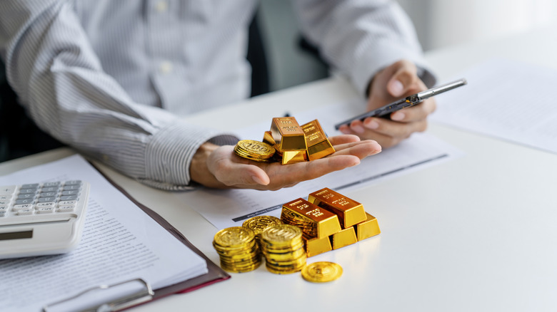 Investor holding gold bars and coins in one hand and a smartphone in another