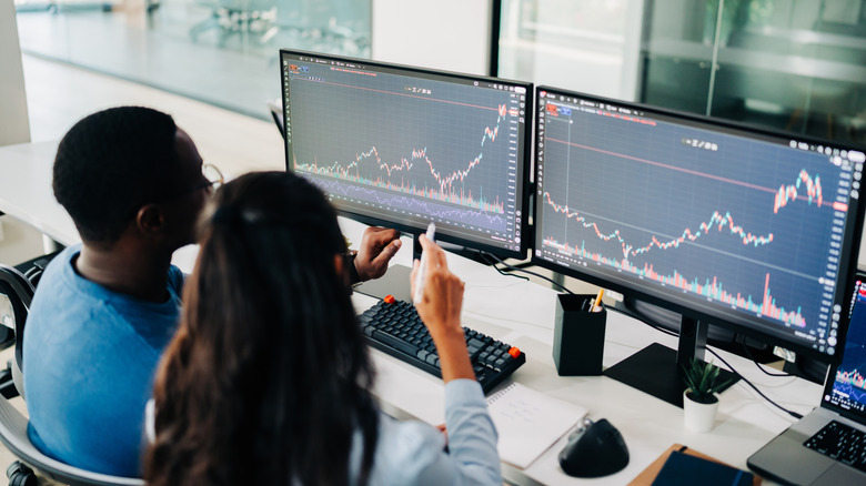 Two people looking at computer screens showing charts