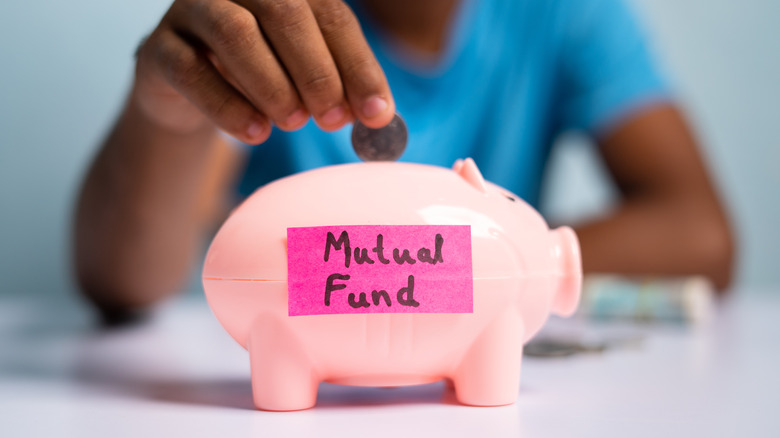 hand putting coin in piggy bank labeled mutual fund
