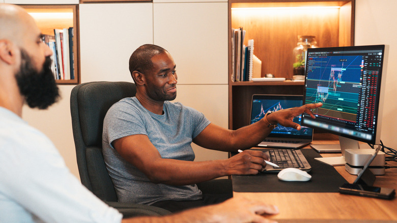 Two investors at a desk, with one showing charts on a computer screen