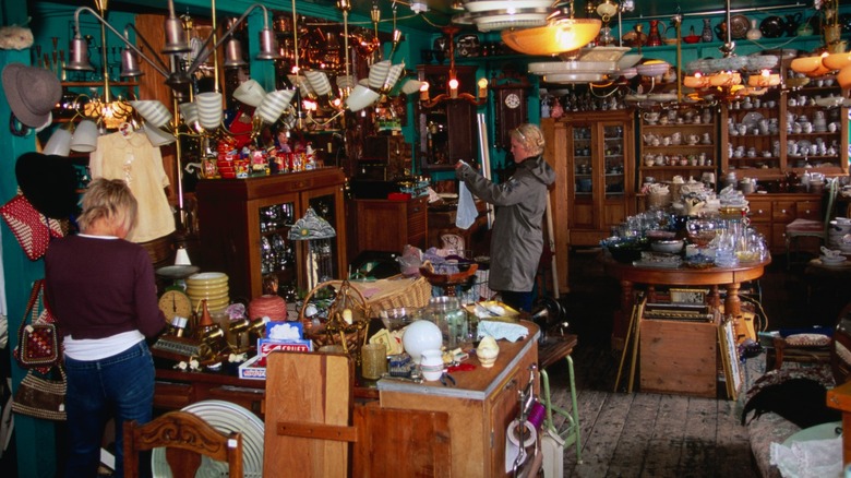 Shoppers at a vintage store with various antiques and collectibles for sale in a small room.