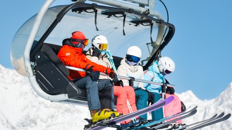 A family of four in brightly colored clothing, helmets, and visors sitting on a ski lift.