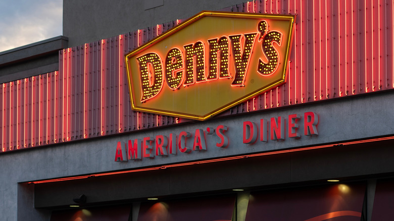 Shot of the front of a Denny's restaurant with its sign lit up in the early evening