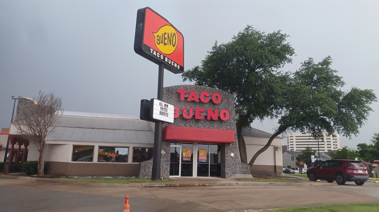 A Taco Bueno with a tall sign and car in the drive-thru line