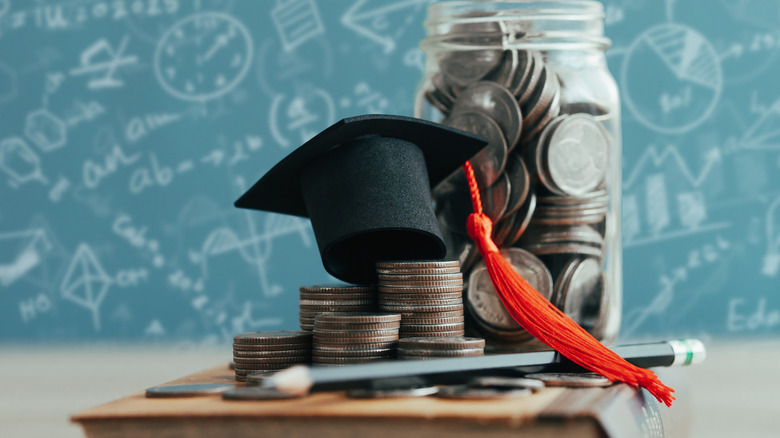 Plies of coins under a tiny graduation hat in front of jar of coins on a book