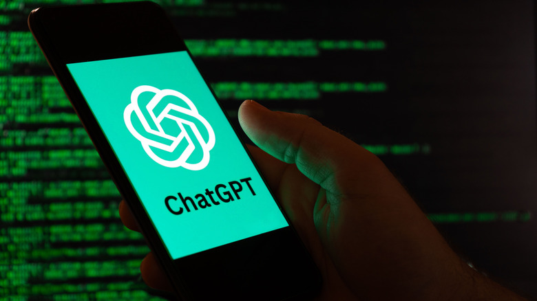 Hand hold a smartphone with the word ChatGPT on the screen, computer code in background