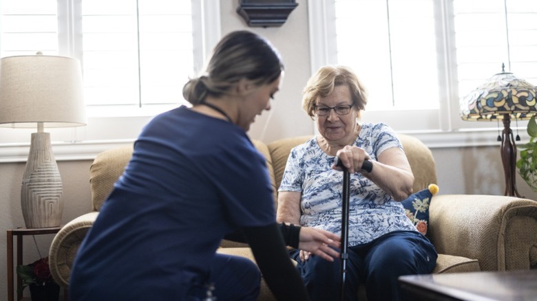 An elderly woman with a cane receiving care from a nurse inside a retirement home.