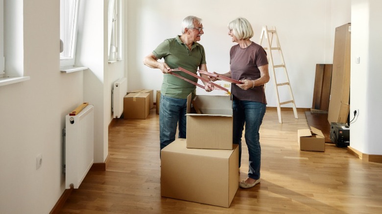 A senior couple packing up their belongings into moving boxes while looking happy.