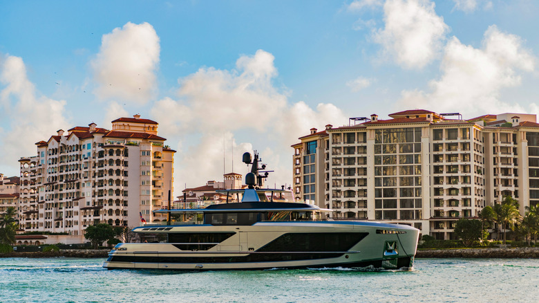 A luxury yacht in the ocean in front of expensive looking apartment buildings.