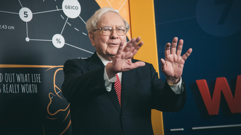 Warren Buffett puts his hands out while addressing a room