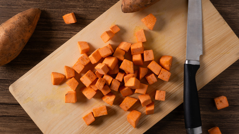 Chopped sweet potato squares next to a kitchen knife, piled up on a cutting board