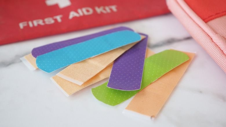 Multi-colored collection of bandaids fanned out on flat surface in front of first aid packet