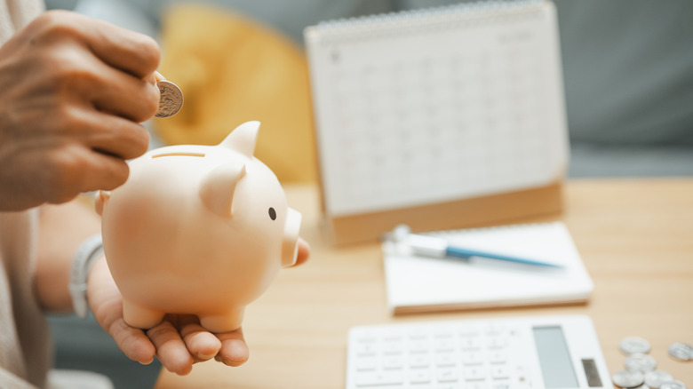 A hand putting a coin in a piggy bank