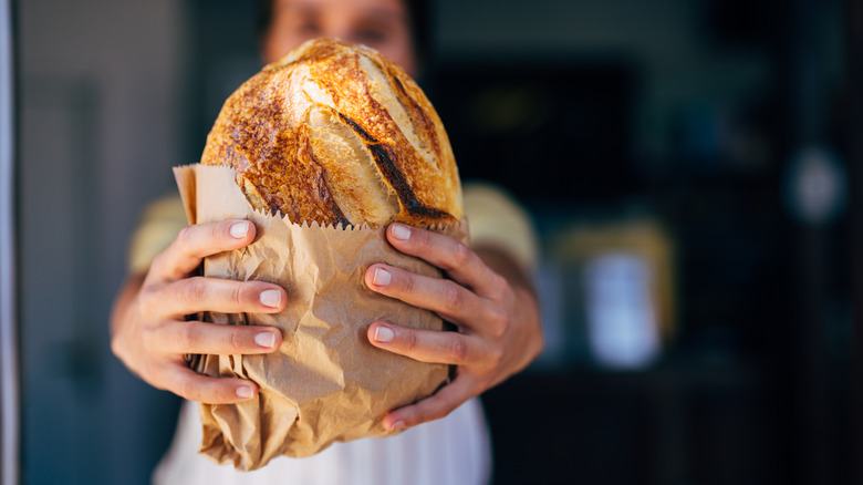 A baker presents a freshly baked artisan bread in a paper bag
