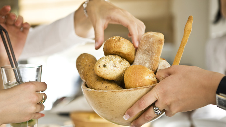 A person being handed a bowl of bread at a table
