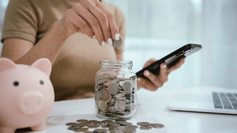 A woman holding a phone and putting coins in a jar