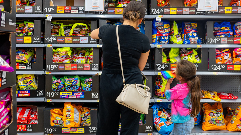 A woman looking at Halloween candy with a child in a store where candy prices are visible.