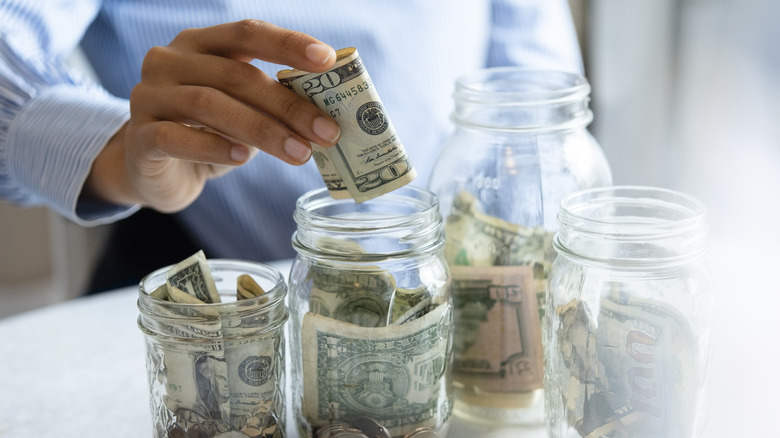 man in dress shirt placing cash in mason jars