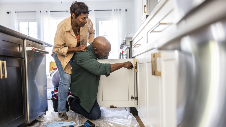 Senior couple repairing kitchen cabinet at home