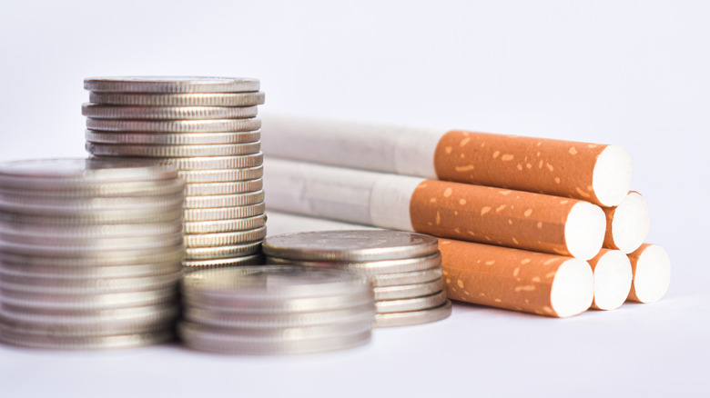 A pyramid of cigarattes next to stacks of silver coins