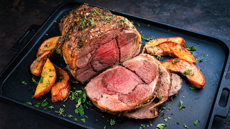 A roasted boneless leg of lamb, sprinkled with herbs, on a baking tray