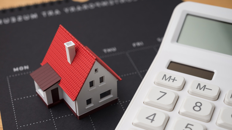 A miniature model home sitting on a calendar next to a calculator.