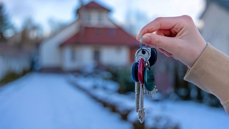 Hand holding a set of house keys in front of a snow-covered home