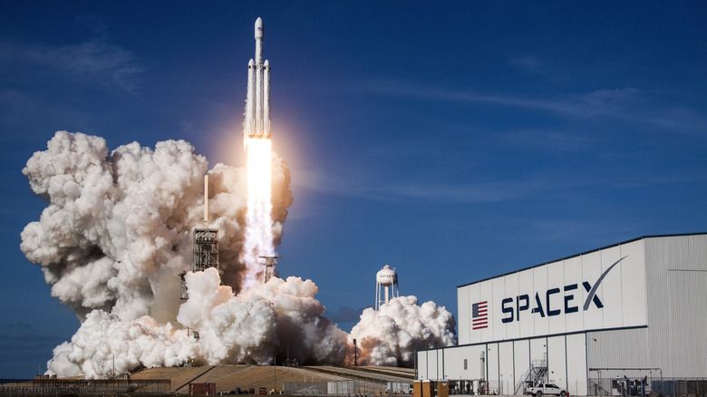 SpaceX building with rocket launch happening behind it.