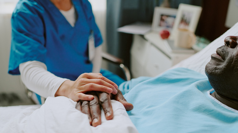 a nurse holds the hand of a man in a hospital bed